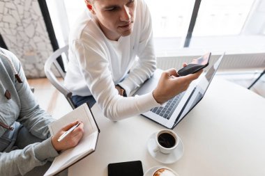 Genç ve yakışıklı işadamı, bir meslektaşıyla iş görüşmesinde ofisinde cep telefonu kullanarak yeni bir finans projesinde başarılar gösteriyor. Takım çalışması..