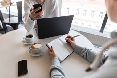 Genç tasarımcı telefonda yeni fikirler ve bir fincan kahve eşliğinde modern bir kafede iş arkadaşına yapılan proje hakkında konuşuyor. İş adamları yeni bir iş projesini tartışıyor. Yakın plan..