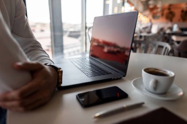 Profesyonel serbest adam kahverengi bir dizüstü bilgisayar ile bir cep telefonundan kahve bir fincan ile modern bir dizüstü bilgisayar ile ofiste bir masada oturan dinleniyor. İşadamı işi düşünüyor.