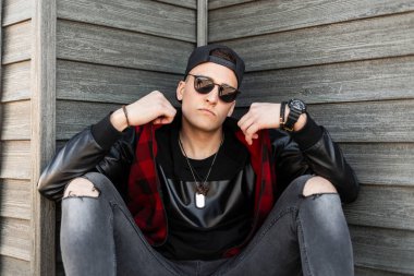 Siyah, modaya uygun, yırtık gri kotlu kırmızı kareli ceketli genç hippi adam eski ahşap evin yanında dinleniyor. Yakışıklı şehir çocuğu dinleniyor. Şık erkek kıyafetleri..