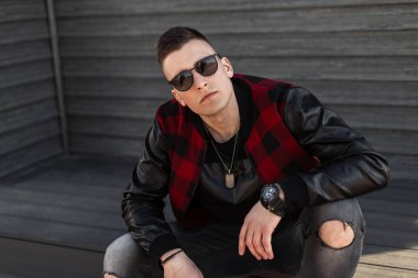 Güneş gözlüklü, modaya uygun bir ceketi olan yırtık kot pantolonlu genç hippi ahşap bir evin yakınındaki klasik merdivenlerde güneşli bir hafta sonunun tadını çıkarıyor. Yakışıklı adam..