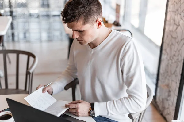 Pohledný mladý podnikatel s laptopem ve stylové košili píše v poznámkovém bloku, který sedí v kavárně. Profesionální Blogger píše nápady. Vzdálená práce. Pohled shora. — Stock fotografie
