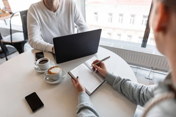 Interviu de angajare - un om de afaceri de succes cu laptop ascultă răspunsurile candidatului. Tânăra femeie manager într-un birou modern care face note într-un notebook . — Fotografie, imagine de stoc