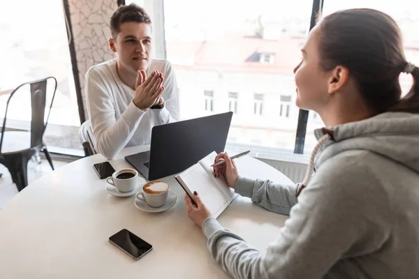 Bonito jovem líder de sucesso em camisa branca fala sobre a empresa e sorri para uma jovem mulher durante uma entrevista. Ambiente de trabalho informal. Recrutamento . — Fotografia de Stock