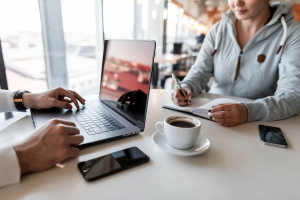 Jovem conversa com seu chefe e toma notas em um bloco de notas. Duas pessoas estão sentadas em um café na mesa branca com café. Entrevista de emprego. Ambiente de trabalho . — Fotografia de Stock