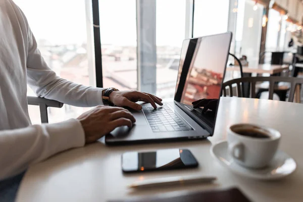 Mladý profesionální svobodný muž v bílé košili pracuje na svém notebooku, zatímco sedí u stolu v kavárně, kde je šálek kávy. Pracovní doba. — Stock fotografie