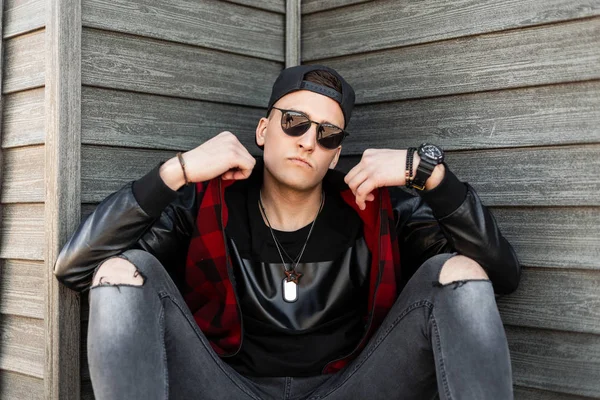 Siyah, modaya uygun, yırtık gri kotlu kırmızı kareli ceketli genç hippi adam eski ahşap evin yanında dinleniyor. Yakışıklı şehir çocuğu dinleniyor. Şık erkek kıyafetleri..