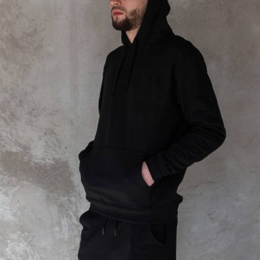 Siyah trendy kot bir Hood ile siyah şık sweatshirt bir sakal ile acımasız yakışıklı genç hipster adam bir Vintage gri duvar yakın poz. Model Amerikalı adam. Erkek moda. Close.