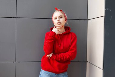 Vintage kot şık bandana bir başlık ile şık bir kırmızı Sweatshirt sarı saçlı güzel seksi genç kadın bir yaz gününde modern bir binada pozlar. Güzel kız. Amerikan tarzı.