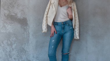 Gri bir duvara yakın metal perçin ile deri moda ceket Vintage yırtık kot şık beyaz tişört ince bir vücut ile genç moda kadın moda modeli. Kadın vücudu yakın çekim.