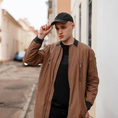 Vintage beyaz binanın yakınında sokakta poz kot siyah bir T-shirt bir siyah moda kap bir bahar şık uzun ceket kendine güvenen şık genç adam. Yürüyüş için modern bir adam. Gençlik.