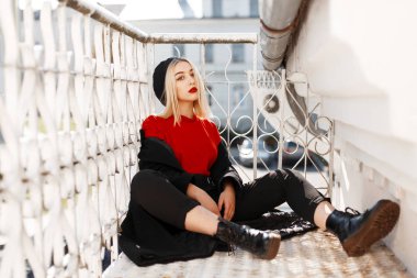 Deri ayakkabı zarif bir Beret şık sonbahar giysileri kırmızı dudaklar ile oldukça güzel genç sarışın kadın Vintage metal korkuluk yakın güneşli bir gün oturur. Şık kız açık havada istirahat.