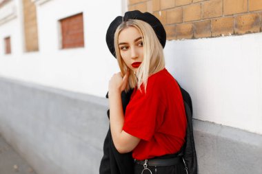 Şık bir Beret şık bir kırmızı t-shirt bir moda siyah ceket seksi dudaklar ile şık güzel modern genç sarışın kadın bir Vintage binanın yakınında şehirde ayakta. Güzel kız.