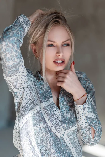 Sexy hübsche junge blonde Frau mit natürlichem Make-up in einem stylischen Hemd mit Vintage-Muster posiert drinnen an einem sonnigen Tag. Nettes schönes Mädchen genießt die Sonnenstrahlen. — Stockfoto