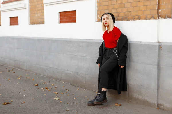세련 된 예쁜 젊은 여자 금발의 긴 검은 코트에서 바지에 빨간 셔츠에 가죽 부츠에 베 레모에서가을 일에 역사적인 건물 근처에 서 휴식. 우아한 여자 야외에서. — 스톡 사진