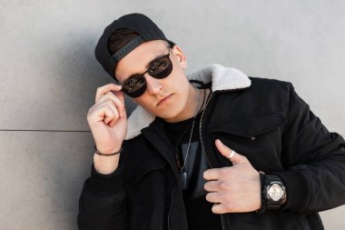 Siyah beysbol şapkalı, modaya uygun siyah gözlüklü ve beyaz yakalı genç Amerikalı hippi modern bir binanın yakınında bir bahar günü için şehre geldi. Kentsel erkek modeli.