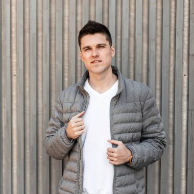 Şık bir saç modeli ile beyaz bir moda t-shirt şık bir gri bahar ceket neşeli genç çekici adam açık havada ahşap vintage duvar yakınında duruyor. Modern Amerikalı adam. Erkek modası.