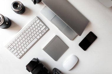 Kamera, dizüstü bilgisayar, klavye, telefon, kablosuz fare ve kamera profesyonel lensler yatıyor beyaz masaüstü üst görünümü. Profesyonel bir fotoğrafçının işyeri. 