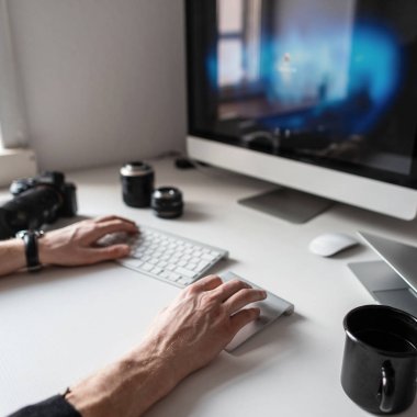 Erkek elleri fotoğraf donanımı ve kahve ile beyaz bir masaüstü bilgisayarda çalışıyor. Adam fotoğrafçı serbest çalışır