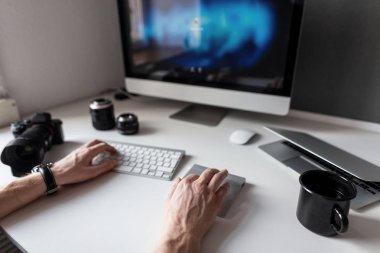 Bilgisayarda çalışan serbest çalışan genç bir fotoğrafçı. Yaratıcı sanat projesi. Kahveli çalışma masası. Klavye, kamera, dizüstü bilgisayar ve lensler. Yaratıcılık sürecinde erkek eller.