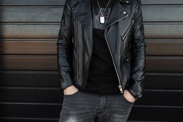 Modischer junger Mann in schwarzer schicker Lederjacke in grauer Vintage-Jeans in stylischem schwarzen T-Shirt posiert vor einer schwarzen Holzwand. neue Kollektion von Herrenbekleidung. Jugendstil. Nahaufnahme. — Stockfoto