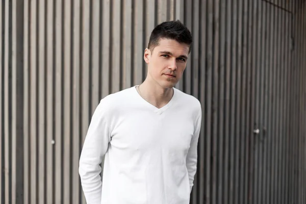 Joven hombre de negocios europeo en una camisa de moda con un peinado elegante se encuentra al aire libre cerca de un edificio de paseo marítimo vintage gris en un día de primavera. Chico guapo modelo . — Foto de Stock