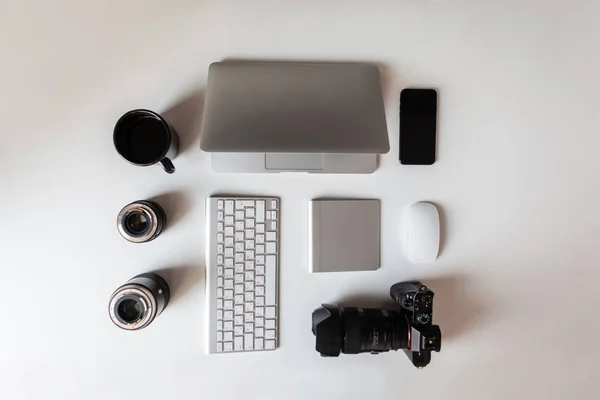 Widok z góry na białym pulpicie, który ma laptopa, obiektywy do kamery, nowoczesny profesjonalny aparat fotograficzny, filiżankę kawy, klawiaturę i telefon. Nowoczesne technologie. — Zdjęcie stockowe
