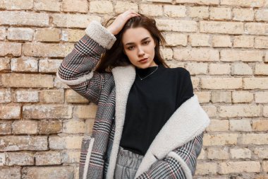 Eski bir tuğla bina açık yakınında poz gri moda pantolon bir vintage damalı ceket siyah bir t-shirt Modern güzel genç esmer kadın. Zarif kız modeli. Bahar stili.