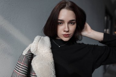 Bir vintage gri duvar kapalı yakın şık bir siyah gömlek kürk ile şık bir damalı ceket doğal makyaj ile sevimli güzel genç esmer kadın Portresi. Güzel kız modeli.