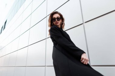 Modern bir açık bina açık havada yakın poz vintage koyu güneş gözlüğü siyah şık bir ceket moda modern hipster genç kadın. Bir yürüyüşte Pretty kentsel güzel kız modeli. Sokak stili.