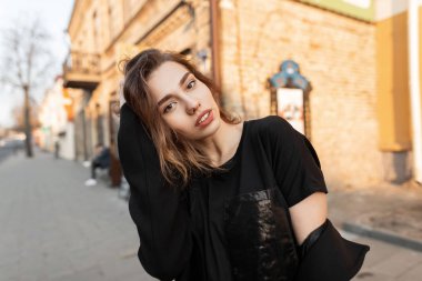 Moda giysiler seksi dudakları ile doğal makyaj ile Oldukça çekici genç kadın gün batımında tuğla vintage evlerin yakınında açık havada pozlar. Güzel şık kız bahar güneşi sahiptir. Sokak stili.