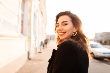Parlak güneşli bir günde şehirde şık bir siyah ceket açık havada sevimli bir gülümseme ile oldukça olumlu güzel genç bir kadının Portresi. Neşeli çekici kız modeli güneşli hafta sonu sahiptir.