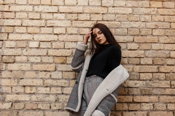 Elegante mujer joven moderna en ropa vintage con estilo retro posando al aire libre en la ciudad cerca de la pared de ladrillo en el día de primavera. Moda hermosa chica modelo de moda . — Foto de Stock