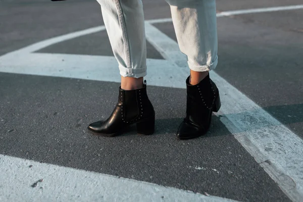 Jambes de femmes en cuir chaussures à talons noirs à la mode dans un jean élégant sur une rue de la ville. Tenue décontractée élégante tendance. Détails du look quotidien. La mode. Gros plan . — Photo