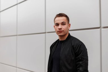 Modern bir binanın yanında duran bir t-shirt şık siyah ceket güzel amerikan yakışıklı genç adam açık havada ayakta. Cool çekici adam model. Sokak rahat tarzı.