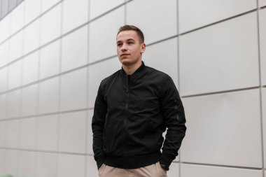 Şehirde modern bir binanın yakınında duran poz moda bir ışık ceket bir saç modeli ile bej şık pantolon Sevimli genç çekici adam. Yakışıklı Avrupalı adam rahatlatıcı.