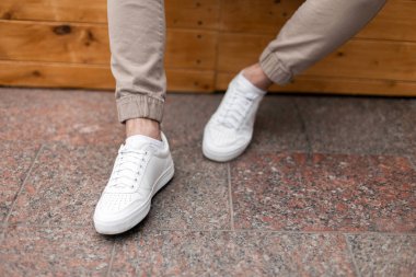 Şık bej pantolon deri moda beyaz spor ayakkabı erkek bacakları. Trendy rahat kıyafet. Günlük görünüşün ayrıntıları. Sokak modası. Close.