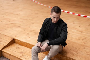 Beyaz spor ayakkabı vintage bej pantolon siyah şık ceket yakışıklı kentsel genç moda adam ahşap adımlar üzerinde oturur ve elektronik modern bir saat bakar. Kapalı çekici Avrupalı adam.