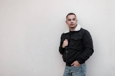 Bir saç modeli ile beyaz kürk ile şık bir ceket mavi şık kot çekici sevimli genç adam şehirde bir duvar ayakın duruyor. Avrupalı bir adam. Trendy erkek giyim.