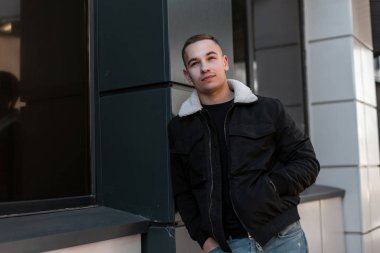 Vintage kot beyaz yakalı şık bir ceket şık bir t-shirt Sevimli kentsel genç adam parlak bir bahar gününde modern bir binanın yakınında ayakta dinleniyor. Şehirde güzel adam.