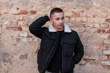 Şık bir saç modeli ile bir t-shirt beyaz yakalı şık bir siyah ceket oldukça yakışıklı genç adam bir tuğla eski binanın yakınında pozlar. Yürüyüş için çekici moda adam. Trendy erkek giyim