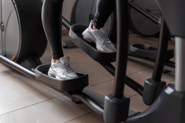 Beyaz spor ayakkabılı kadın bacakları spor salonundaki stepper simülatöründe çalışıyor. Sağlık kulübünde egzersiz yapan bir kız. Yakın plan..