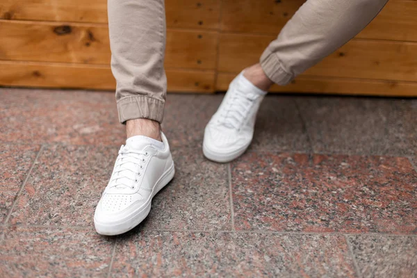 Männerbeine in Ledermode weiße Turnschuhe in schicken beigen Hosen. trendiges Casual Outfit. Details des täglichen Aussehens. Straßenmode. Nahaufnahme. — Stockfoto