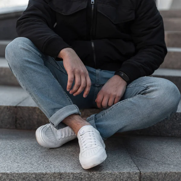 Benen van een jonge man in blauwe jeans in stijlvolle witte leren sneakers. Stijlvolle heren schoenen. Casual design. Close-up van mannelijke benen. — Stockfoto