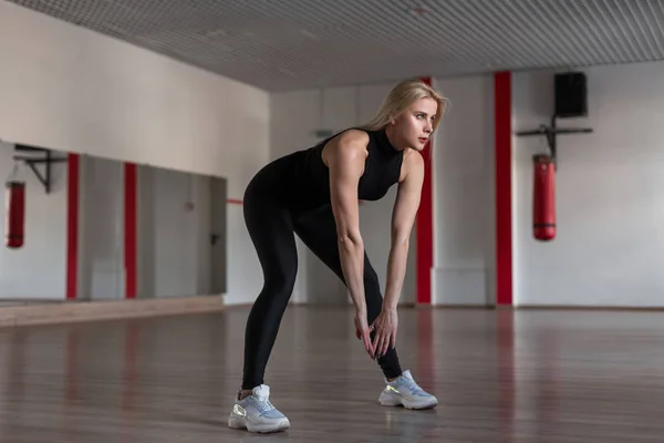 Ung smal atletisk kvinna i sportig svart fashionabla kläder på en träning i gymmet. Attraktiv tjej gör övningarna i träningsstudion. En hälsosam livsstil. — Stockfoto