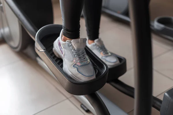 As pernas femininas em tênis brancos na moda estão andando em um simulador de passo em um estúdio de fitness. Jovem treina em um ginásio moderno. Conceito de esportes e saúde. Close-up . — Fotografia de Stock