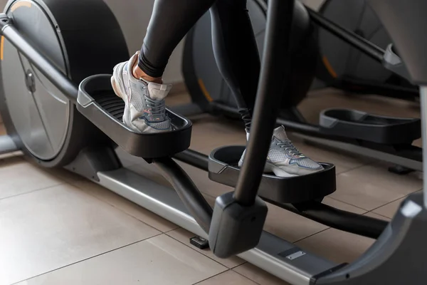 Mujer joven camina en ropa deportiva en el simulador de pasos en el gimnasio. Chica hace ejercicios de ejercicio cardiovascular. Estilo de vida saludable. Primer plano del simulador y las piernas de las mujeres . — Foto de Stock