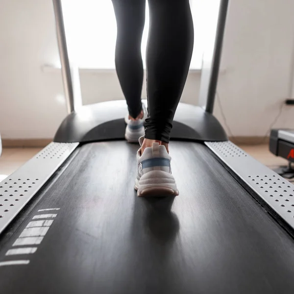 Mulher esportiva jovem atraente trabalhando no ginásio. A rapariga está a treinar cardiologia em esteira. Caminhando em uma esteira. Vista traseira. Fechar as pernas femininas . — Fotografia de Stock