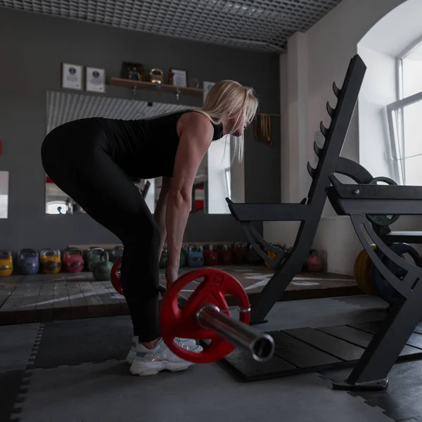 Mujer joven perfecta con un cuerpo deportivo está haciendo ejercicios con una barra en el gimnasio. Chica entrena con una barra en el interior . —  Fotos de Stock
