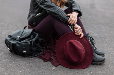 Kaldırımda zarif bir şapka ile bir deri sırt çantası ile moda çizmeler mor pantolon siyah şık ceket genç bir kadın oturur. Kadın giyim yeni moda koleksiyonu. Close.